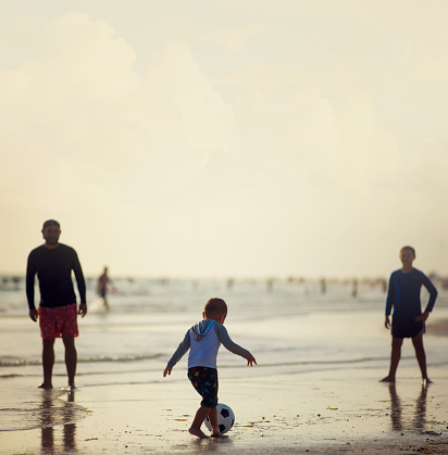 Family of three playing soccer in the beach