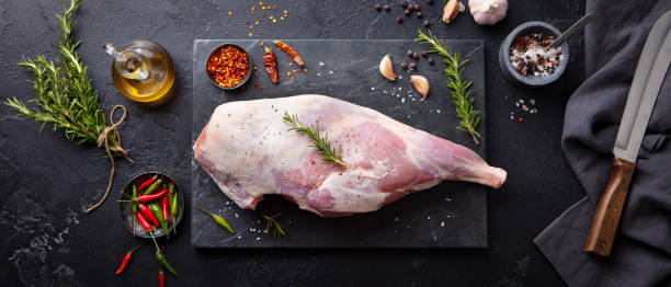 istock Raw lamb leg with spices and herbs on marble cutting board. Dark background. Top view. 1255463974