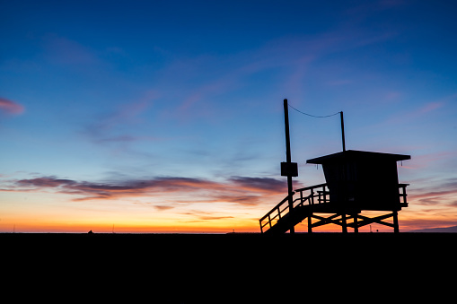 Silhouette of lifeguard tower with colorful sunset and clouds in the back drop
