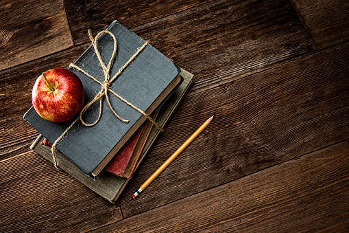 This is a photograph of a red apple on top of a stack of old retro books held together with twine sitting on top of a old retro wooden table