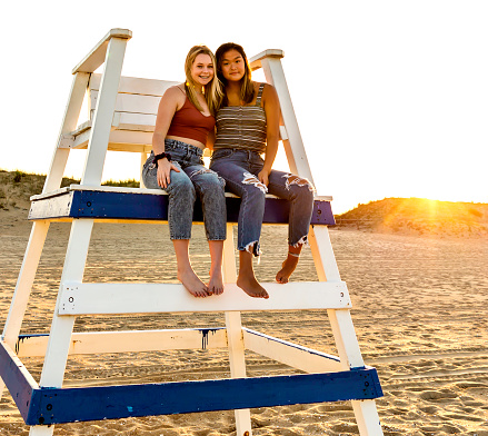 Teen girls sit in oversized lifeguard chair at the beach