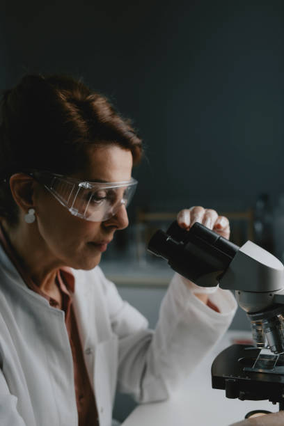 senior female scientist/lab technician doing research by using a microscope - lab coat women one person female stock-fotos und bilder