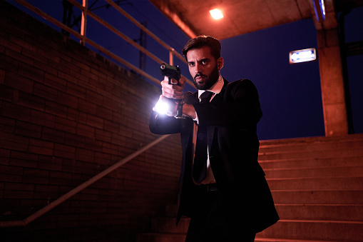 Secret service special agent working at night on a train railroad station in a tuxedo suit, carrying a gun.
