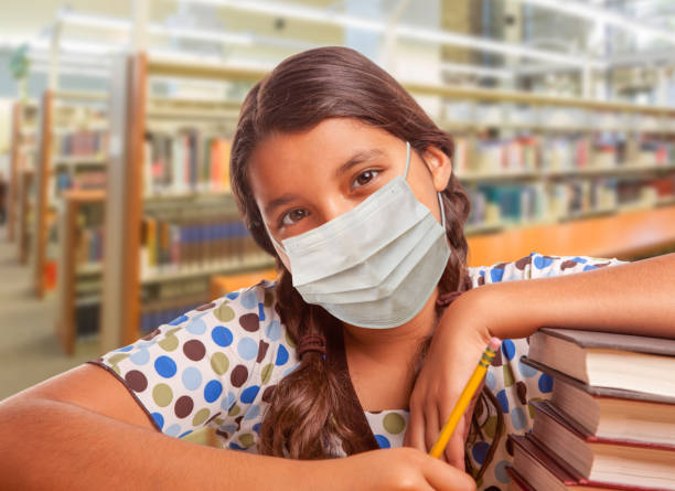 istock Hispanic Girl Student Wearing Face Mask Studying in Library 1255481234
