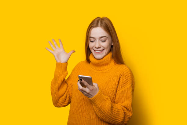 Caucasian ginger girl with freckles gesturing a win holding a mobile and posing in a warm sweater on a yellow background Caucasian ginger girl with freckles gesturing a win holding a mobile and posing in a warm sweater on a yellow background moldova photos stock pictures, royalty-free photos & images