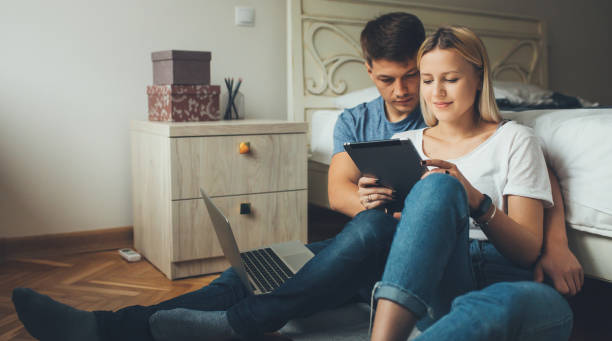istock Young caucasian couple planning something while using a tablet and notebook on the floor in the bedroom 1255508018