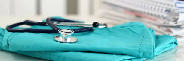 Photo of Medical stethoscope lying on green doctor uniform closeup
