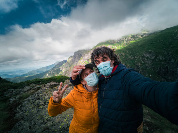 A cheerful couple tourists relaxing in the Nature. Casual Clothing. Weekend Activities. Hiking in the highlands at the end of the quarantine of COVID-19. de vuelta a la naturaleza. la nueva normalidad. retrato de una pareja feliz turistas con máscara protectora en sus rostros senderismo en las montañas. disfrute al aire libre en un día soleado durante la pandemia covid-19. saludar a tus amigos en las red