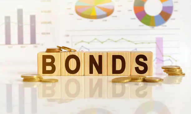 Photo of Bonds the word on wooden cubes, cubes stand on a reflective surface, in the background is a business diagram.