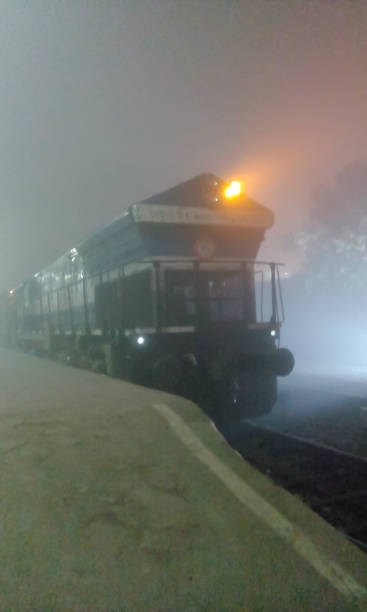 列車は夜に空の鉄道駅で停止しました。インドの鉄道駅プラットフォームは、通勤者がいない霧の多い冬の夜に異なって見えます。 マルダ タウン インディア - locomotive train night vertical ストックフォトと画像