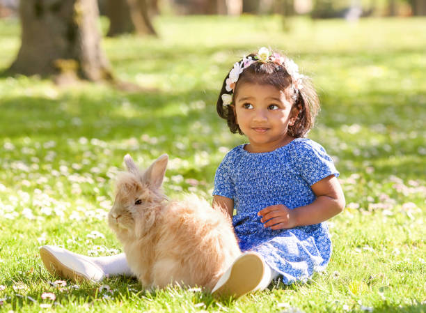 istock A small  girl is sitting with rabbit on green grass in spring park 1255533095