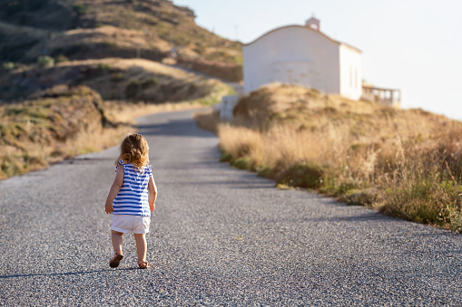 A little toddler girl walks alone on an empty street during sunset time