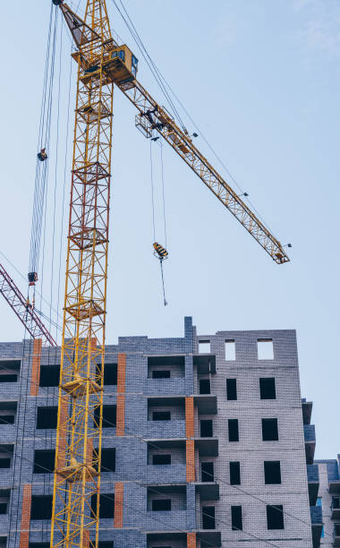 istock Modern building under construction with crane. From below of constructing building with high crane under clear sky 1255536304