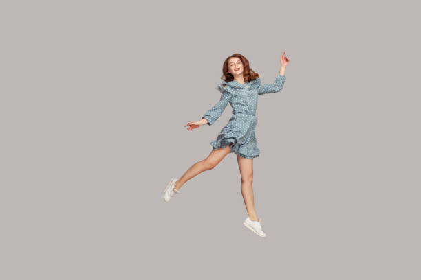 Happy delicate girl in vintage ruffle dress levitating with ballet dance move, hovering in mid-air and smiling joyfully Happy delicate girl in vintage ruffle dress levitating with ballet dance move, hovering in mid-air and smiling joyfully, jumping trampoline, flying up. indoor studio shot isolated on gray background zero gravity stock pictures, royalty-free photos & images