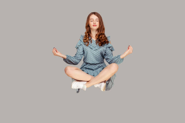 hovering in air. calm peaceful relaxed girl ruffle dress levitating with mudra gesture hands up, closed eyes, meditating - levitation imagens e fotografias de stock