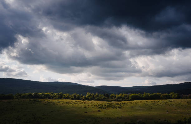 istock Dramatic sky with dark rain clouds and sunshine illuminating green slopes 1255537512