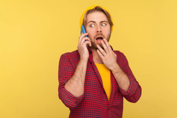 istock Surprised trendy guy in hipster beanie hat and checkered shirt calling, expressing shock emotions while talking mobile phone 1255537838
