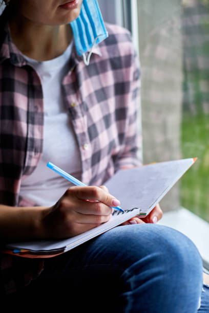 istock Woman sitting at the window, writing in notebook plan, to do list after quarantine end, coronovirus ending 1255542408
