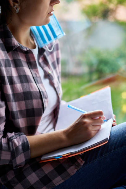 istock Woman sitting at the window, writing in notebook plan, to do list after quarantine end, coronovirus ending 1255542409