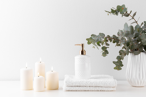 Stack of white bath towels, soap, bouquet of eucalyptus and candles over pastel background