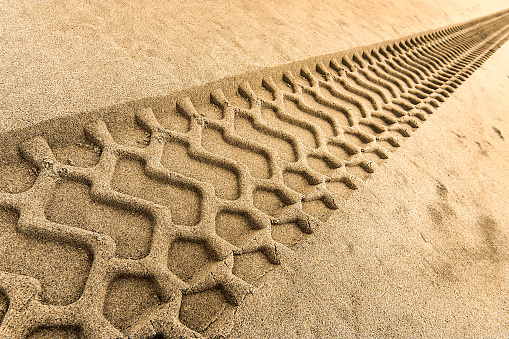 Close-up of a diagonal tire tread pattern from a construction machine in sand on a roadworks site.