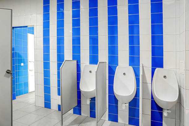 A elongated white toilet with the seat lid in the up position. The toilet is highlighted with a spot light coming from above. This sparse room has blue-green walls and a dark hardwood floor.