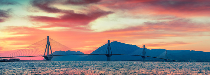 Dramatic evening sunset with Rion-Antirion Bridge. Colorful spring panorama of the Gulf of Corinth, Greece, Europe. Beauty of countryside concept background. Artistic style post processed photo.
