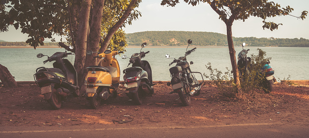 Scooters are parked on the side of the road near the sea or ocean