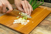 Women's hands cut green onions with a knife on a wooden Board close up