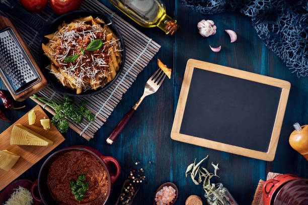 istock Penne with Bolognese sauce in serving size casserole with ingredients in rustic pots with a blackboard 1255563590