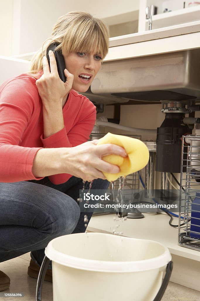 Mulher com limpar a pia com vazamento no telefone para Encanador - Foto de stock de Encanador royalty-free