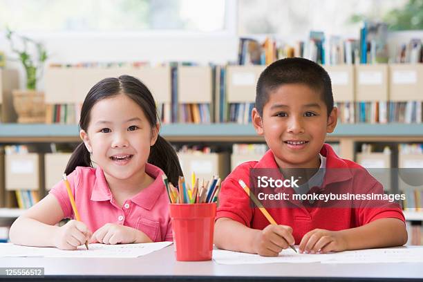 Kindergarten Children Sitting At Desk And Writing Stock Photo - Download Image Now - Looking At Camera, Preschool, Writing - Activity