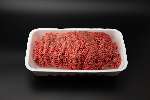 Raw minced (ground) meat in a white styrofoam container isolated on black background with copy space for text