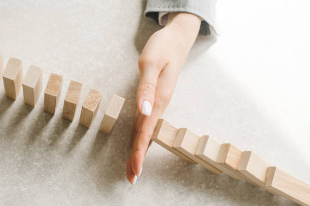 la mano della ragazza in una giacca grigia ferma la caduta di blocchi di legno. gestione delle crisi - change changing form organization leadership foto e immagini stock