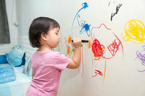 little baby  girl drawing with crayon color on the wall