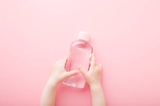 Baby girl little hands holding transparent plastic bottle of oil on light pink table background. Pastel color. Care about soft body skin. Closeup. Point of view shot. Top down view. Baby girl little hands holding transparent plastic bottle of oil on light pink table background. Pastel color. Care about soft body skin. Closeup. Point of view shot. Top down view. massage oil photos stock pictures, royalty-free photos & images