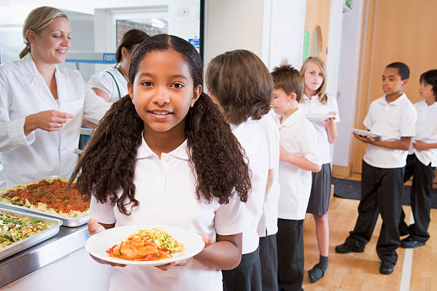 Schoolgirl holding plate of lunch in school cafeteria Schoolgirl holding plate of lunch standing at end of queue in school cafeteria cafeteria school lunch education school stock pictures, royalty-free photos & images