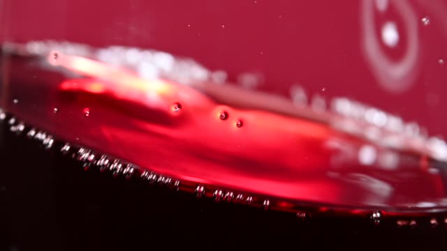 Close up swirling red wine in wineglass over red