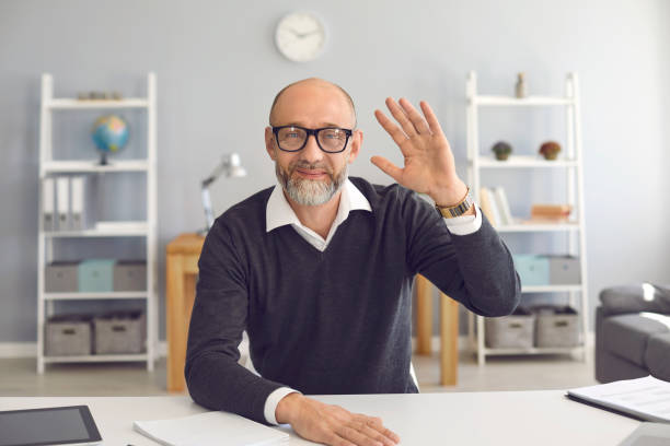 istock Waving old businessman smiling looking at the camera video call web camera gadget sitting in the apartment. 1255580407