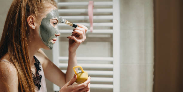 istock Ginger lady in front of the mirror applying a facial mask using special tools 1255580774