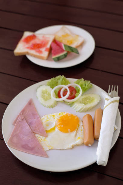 istock American breakfast - fried egg , sausage , ham and toasts with strawberry jam  on wihte plate on wood table 1255582927