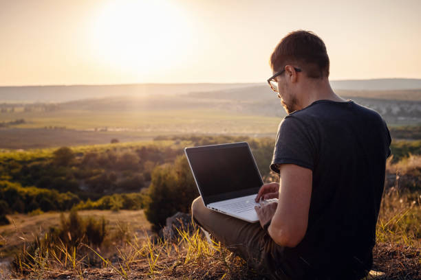 hombre con portátil sentado en el borde de una montaña con impresionantes vistas del valle - hipster people surfing the net internet fotografías e imágenes de stock