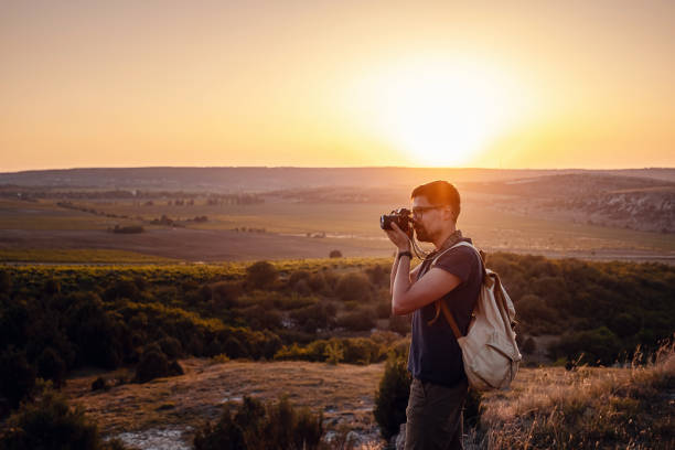 Man photographer with backpack and camera taking photo of sunset mountains Travel Lifestyle hobby concept adventure active vacations outdoor