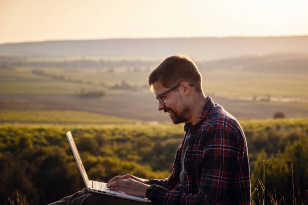 hombre con portátil sentado en el borde de una montaña con impresionantes vistas del valle - hipster people surfing the net internet fotografías e imágenes de stock