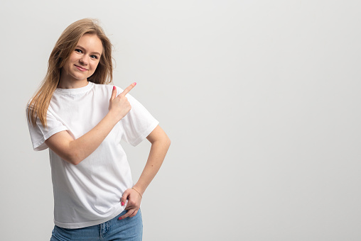 Portrait of young caucasian blonde woman pointing at white background with finger. banner. copy space
