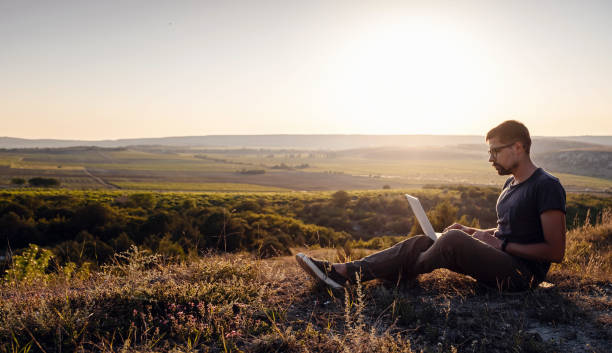 hombre con portátil sentado en el borde de una montaña con impresionantes vistas del valle - hipster people surfing the net internet fotografías e imágenes de stock