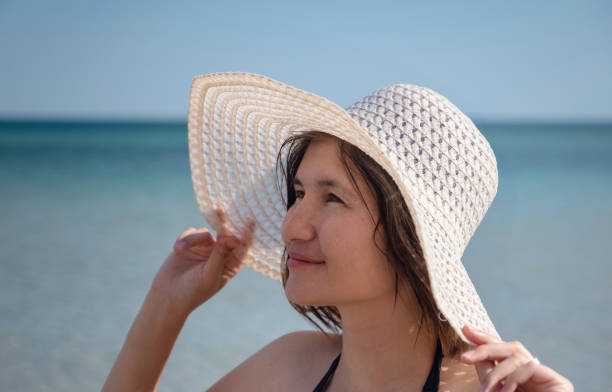 istock Beautiful Young Woman At Beach Wearing Hat 1255588069