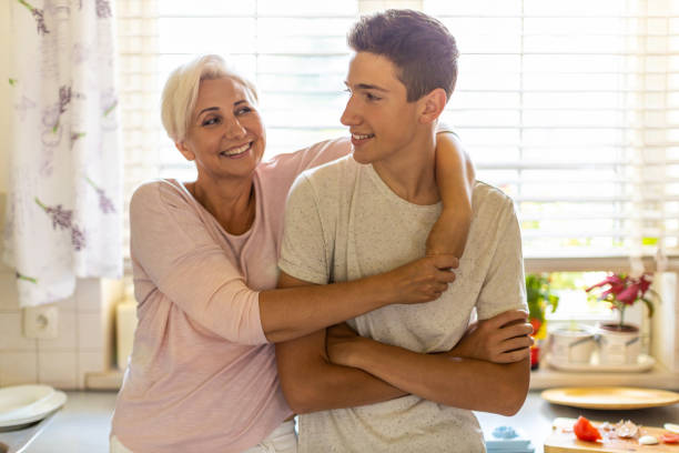 moeder die haar tienerzoon in de keuken koestert - zoon stockfoto's en -beelden