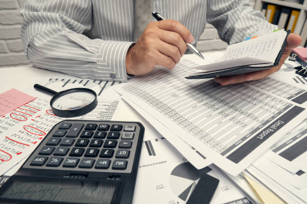 istock Business analysis and accounting concept - businessman working with document, spreadsheet, using calculator, tablet pc. Office desk closeup. 1255594337