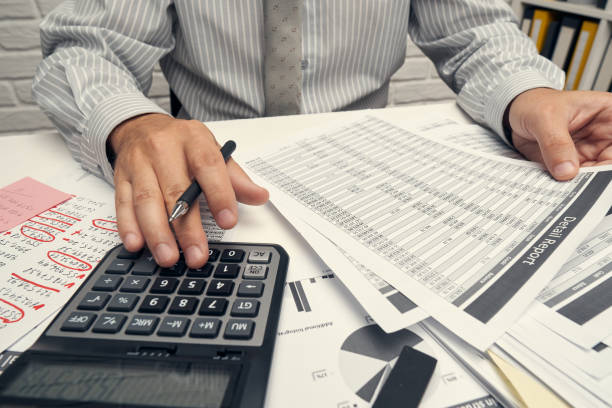 istock Business analysis and accounting concept - businessman working with document, spreadsheet, using calculator, tablet pc. Office desk closeup. 1255594369